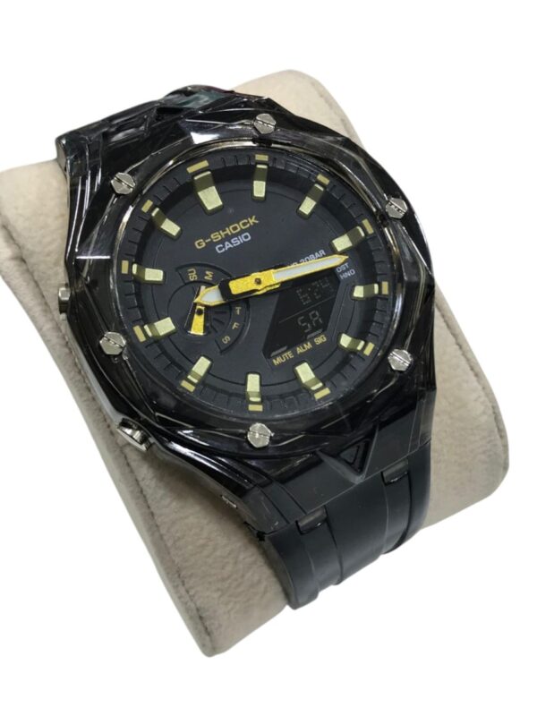 ساعة G-SHOCK CasiOak معدلة بإطار وكفة شفافة ومينا طيفي بألوان الطيف الأزرق والأرجواني (Rainbow Dial) على حامل عرض بيج.